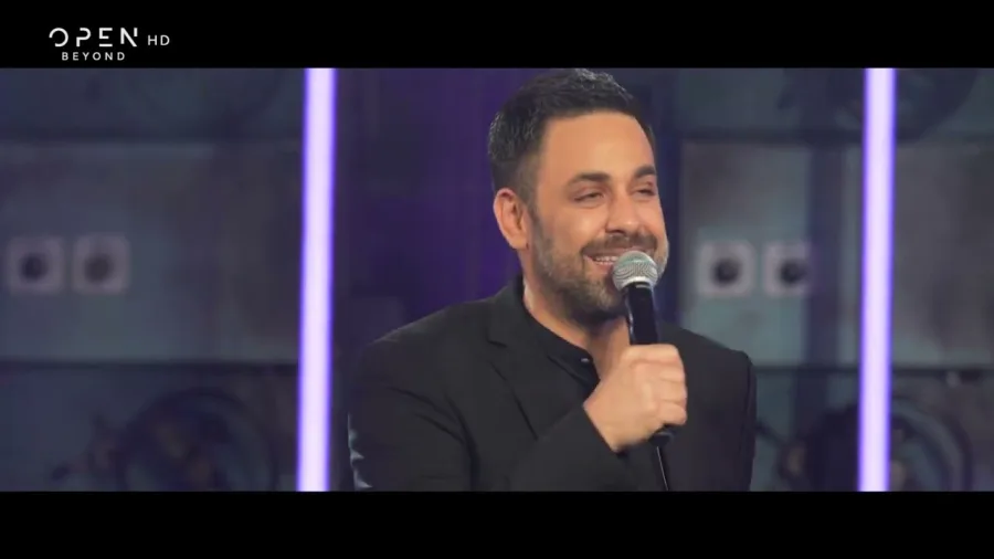 Ο Γιώργος Γιαννιάς τραγουδάει σε τηλεοπτική εκπομπή κρατώντας μικρόφωνο.