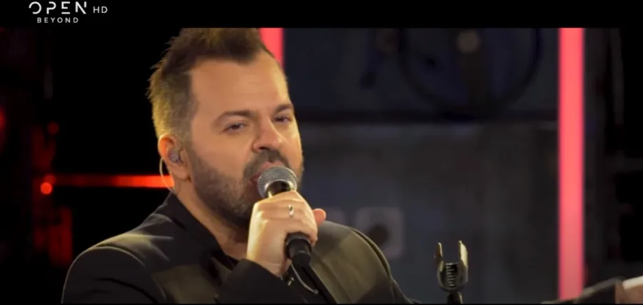 Ο Νίκος Απέργης τραγουδάει σε σκηνή κρατώντας μικρόφωνο.