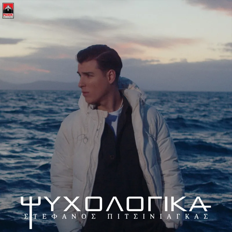 Ο Στέφανος Πιτσίνιαγκας με λευκό μπουφάν μπροστά από τη θάλασσα.
