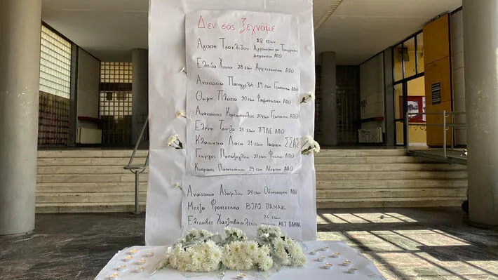 Χειρόγραφη λίστα με ονόματα φοιτητών και λουλούδια σε φουαγιέ πανεπιστημίου.