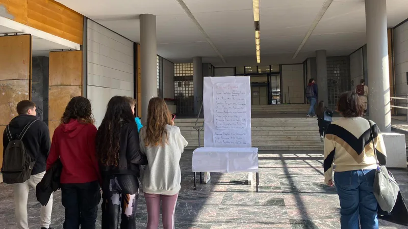 Φοιτητές του ΑΠΘ μπροστά από λίστα με ονόματα θυμάτων των Τεμπών στο φουαγιέ.