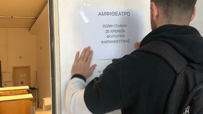 Φοιτητής κολλάει χαρτί σε τοίχο αμφιθεάτρου στη μνήμη θύματος των Τεμπών.