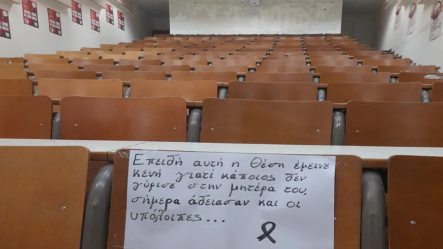 Άδειο αμφιθέατρο πανεπιστημίου με χειρόγραφο σημείωμα σε ένα έδρανο για την τραγωδία στα Τέμπη.