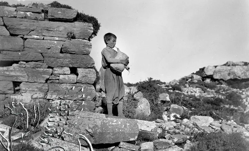 Αγόρι που παίζει τσαμπούνα δίπλα σε πέτρινο τοίχο.