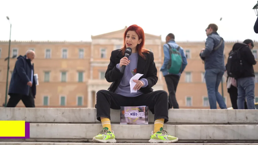 Η Σοφία Θεοδώρα Γιλτίζη κάθεται σε σκαλιά κρατώντας μικρόφωνο και χαρτιά.