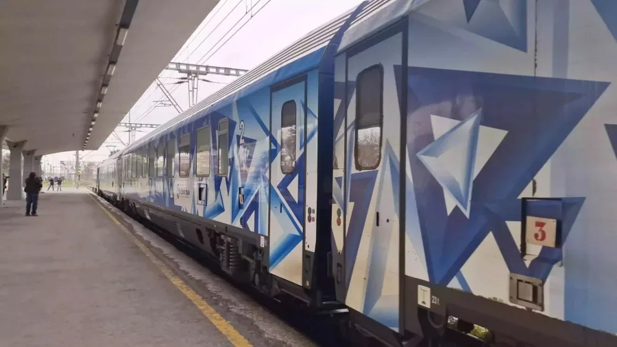 Τρένο της Hellenic Train με μπλε γεωμετρικά σχέδια σταματημένο σε αποβάθρα σιδηροδρομικού σταθμού.