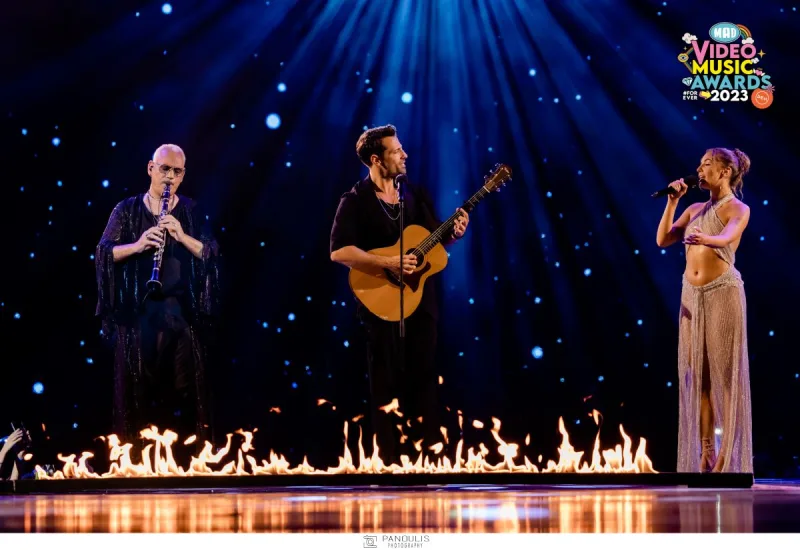 Τρεις καλλιτέχνες στη σκηνή των Mad VMA 2023 με φωτιές και μπλε φωτισμό.