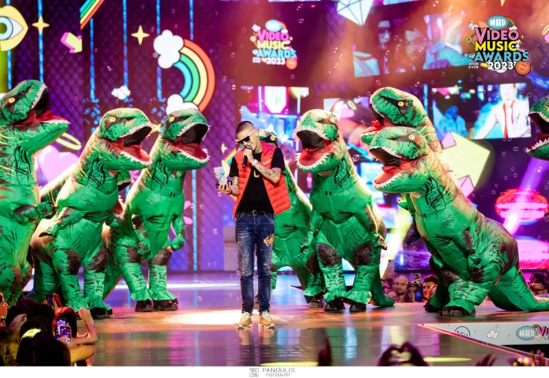 Καλλιτέχνης στη σκηνή των Mad Video Music Awards 2023 περιτριγυρισμένος από άτομα με στολές δεινοσαύρων.