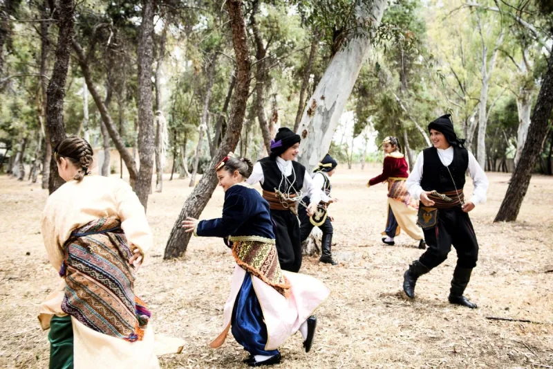 Παιδιά με παραδοσιακές ελληνικές στολές χορεύουν σε δάσος.