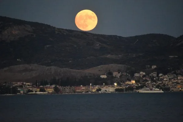 Η Μπλε Πανσέληνος πάνω από βουνό και παραθαλάσσια πόλη.