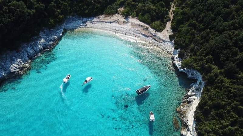 Αεροφωτογραφία από παραλία στους Παξούς με γαλαζοπράσινα νερά και σκάφη.