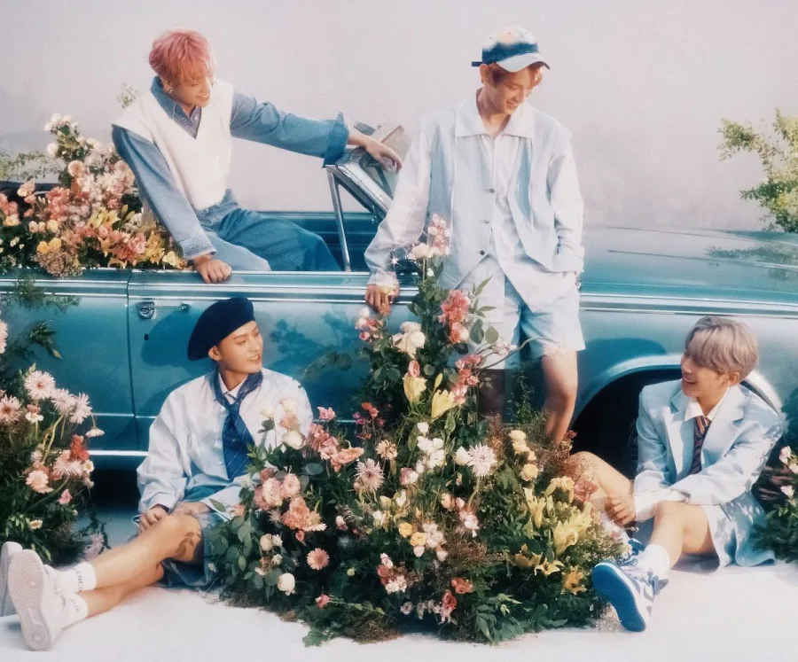 Το K-pop συγκρότημα LUMINOUS ποζάρει γύρω από ένα γαλάζιο αυτοκίνητο με λουλούδια.