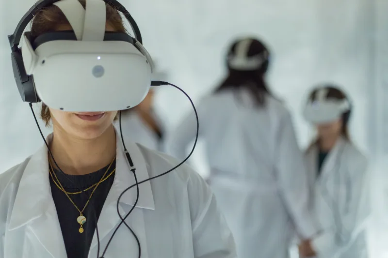 Άτομα με λευκές ιατρικές ποδιές φορούν VR headsets σε εγκατάσταση εικονικής πραγματικότητας.