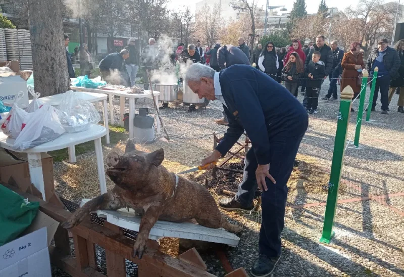 Άνδρας προετοιμάζει παραδοσιακό χοιρινό σε υπαίθρια εκδήλωση για τα Χριστούγεννα.