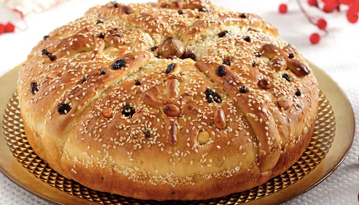 Χριστόψωμο στολισμένο με σουσάμι, καρύδια και σταφίδες σε χρυσό δίσκο.