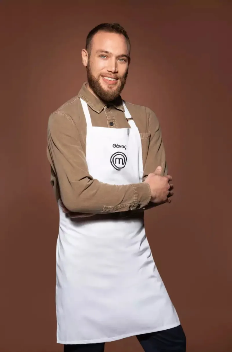 Ο Θάνος, παίκτης του MasterChef, ποζάρει με λευκή ποδιά και καφέ πουκάμισο.