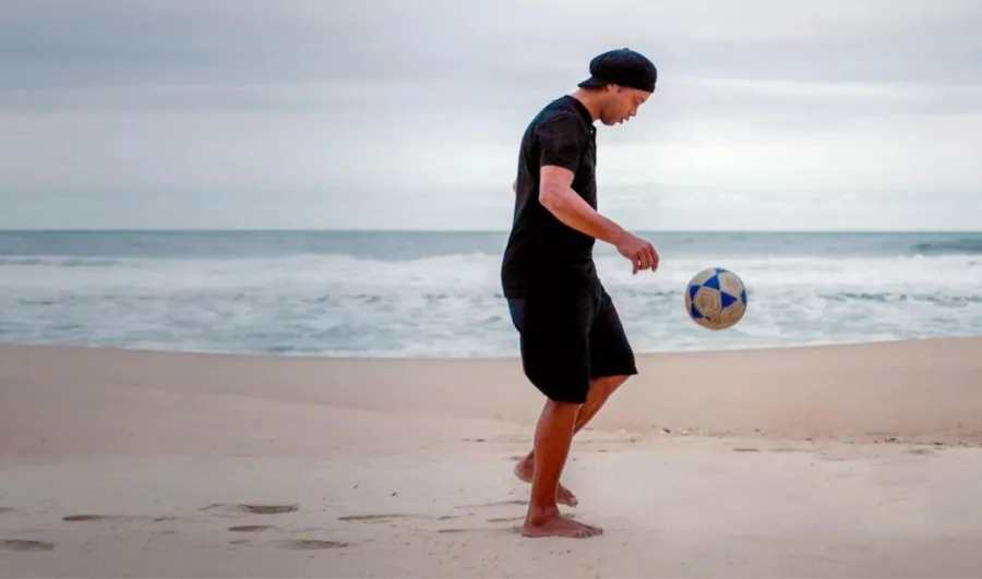 Ο Ronaldinho παίζει ποδόσφαιρο σε μια παραλία.