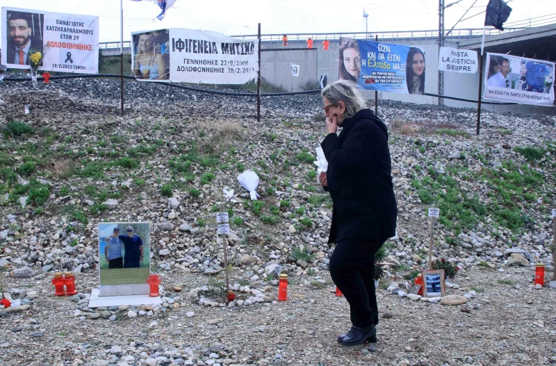 Γυναίκα με μαύρα ρούχα σε σημείο μνήμης με φωτογραφίες και πανό για τα θύματα των Τεμπών.