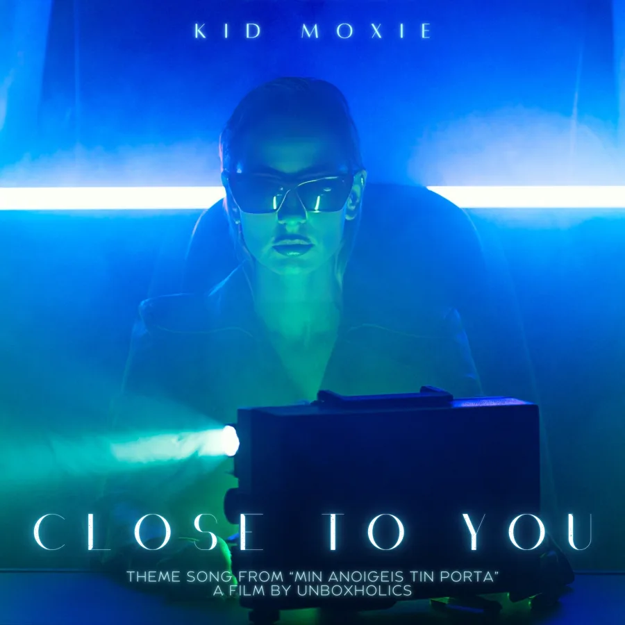 Η Kid Moxie με γυαλιά ηλίου μπροστά από έναν προβολέα σε μπλε φωτισμό.