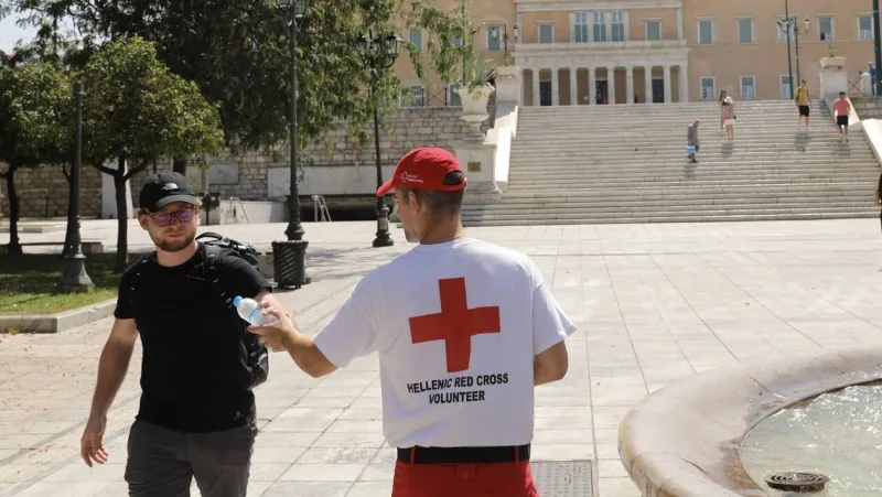 Εθελοντής του Ελληνικού Ερυθρού Σταυρού προσφέρει μπουκάλι νερό σε περαστικό στην Πλατεία Συντάγματος.