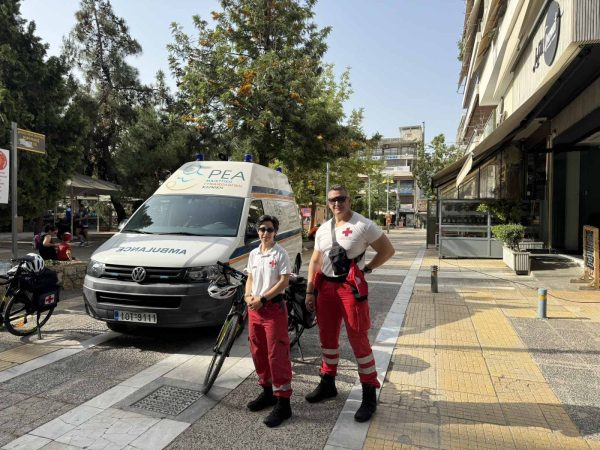 Δύο εθελοντές του Ελληνικού Ερυθρού Σταυρού μπροστά από ασθενοφόρο σε πεζόδρομο.