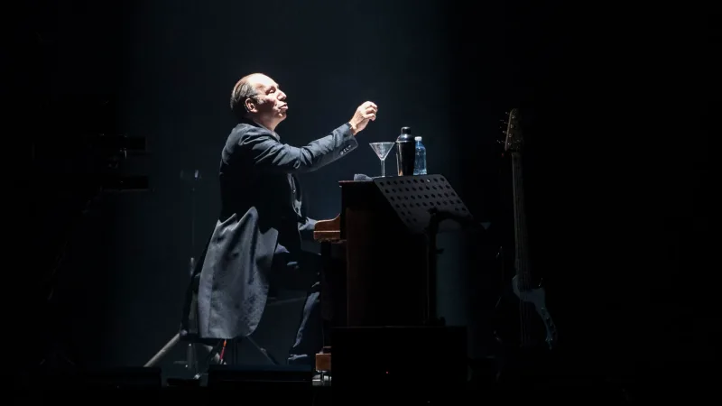 Ο Hans Zimmer σε συναυλία παίζοντας πιάνο σε σκοτεινή σκηνή.