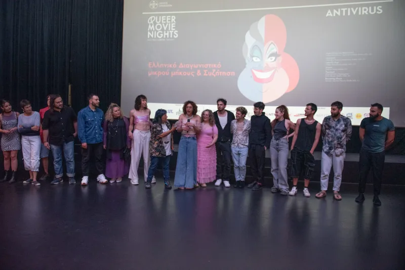 Ομάδα ανθρώπων στη σκηνή του Queer Movie Nights 2024 μπροστά από οθόνη προβολής.