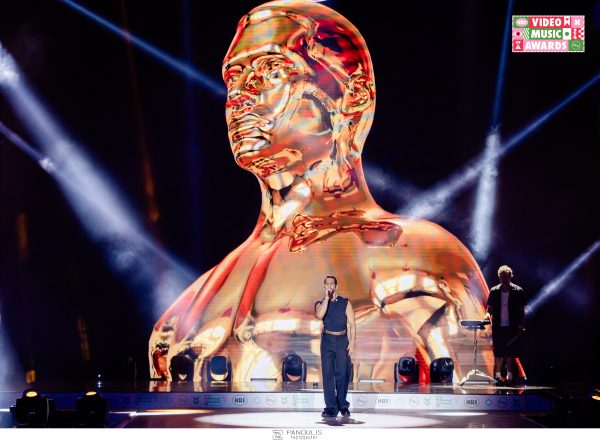 Καλλιτέχνης στη σκηνή των Mad VMA 2024 μπροστά από γιγαντιαία χρυσή προτομή.