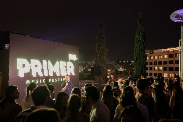Παρουσίαση του Primer Music Festival σε ταράτσα με κόσμο και μεγάλη οθόνη.