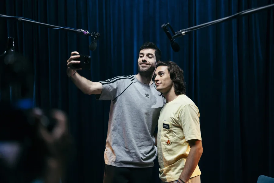Δύο άνδρες βγάζουν selfie σε στούντιο με μπλε κουρτίνα.