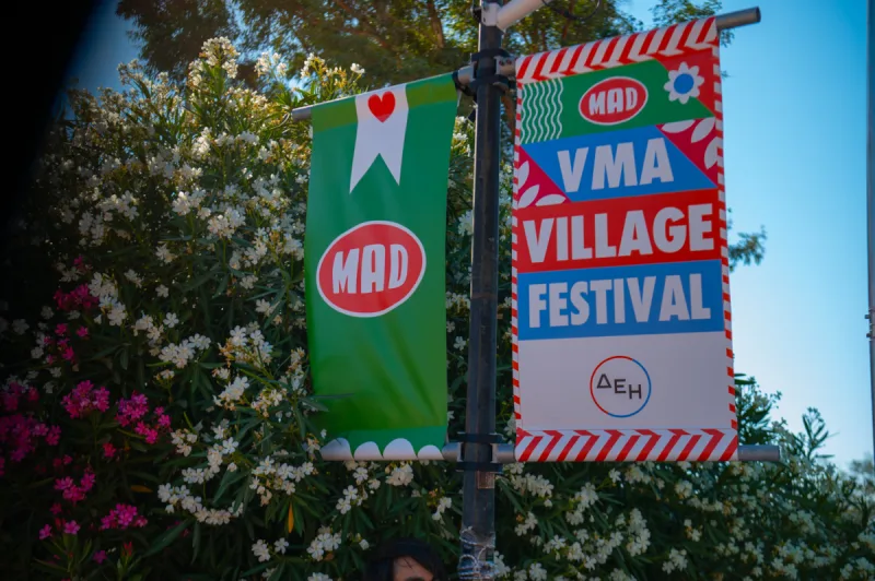 Λάβαρα του Mad VMA Village Festival από την ΔΕΗ σε εξωτερικό χώρο με λουλούδια.