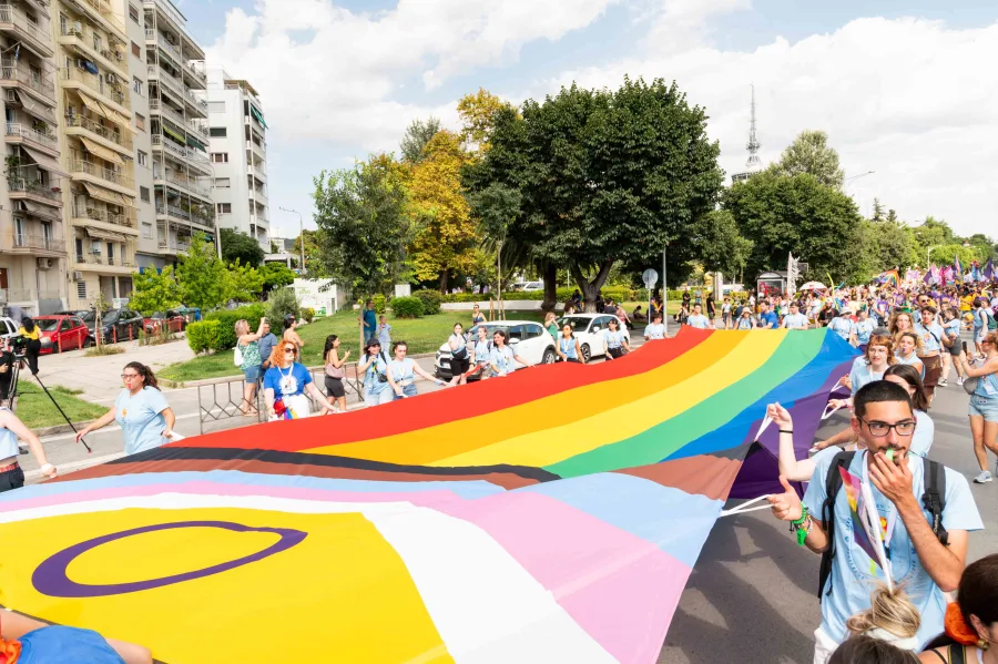 Πλήθος κόσμου κρατά μια τεράστια σημαία Progress Pride στην παρέλαση του EuroPride 2024.