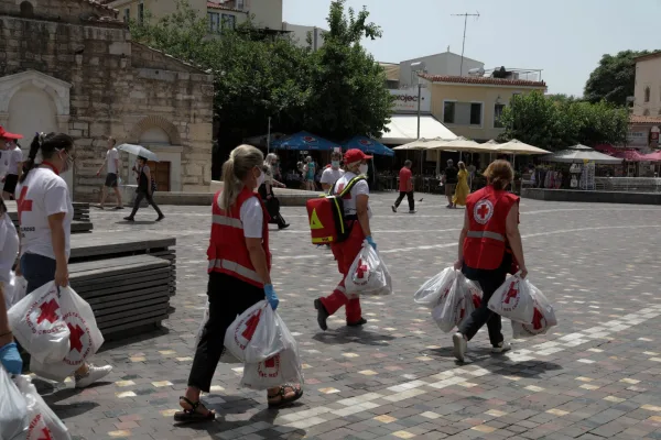 Εθελοντές του Ελληνικού Ερυθρού Σταυρού σε πλατεία της Αθήνας κρατώντας τσάντες με εφόδια.