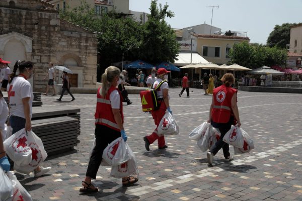 Εθελοντές του Ελληνικού Ερυθρού Σταυρού σε πλατεία της Αθήνας κρατώντας τσάντες με εφόδια.