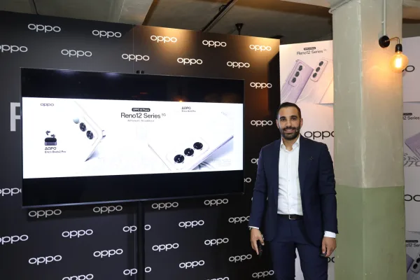 Άνδρας με κοστούμι δίπλα σε οθόνη παρουσίασης της σειράς OPPO Reno12.