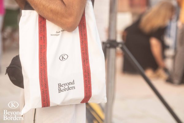 Λευκή υφασμάτινη τσάντα με το λογότυπο Beyond Borders και κόκκινες λεπτομέρειες.