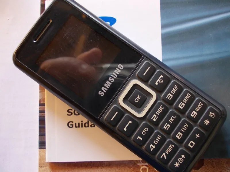 Κλασικό κινητό τηλέφωνο Samsung με κουμπιά πάνω σε εγχειρίδιο οδηγιών.