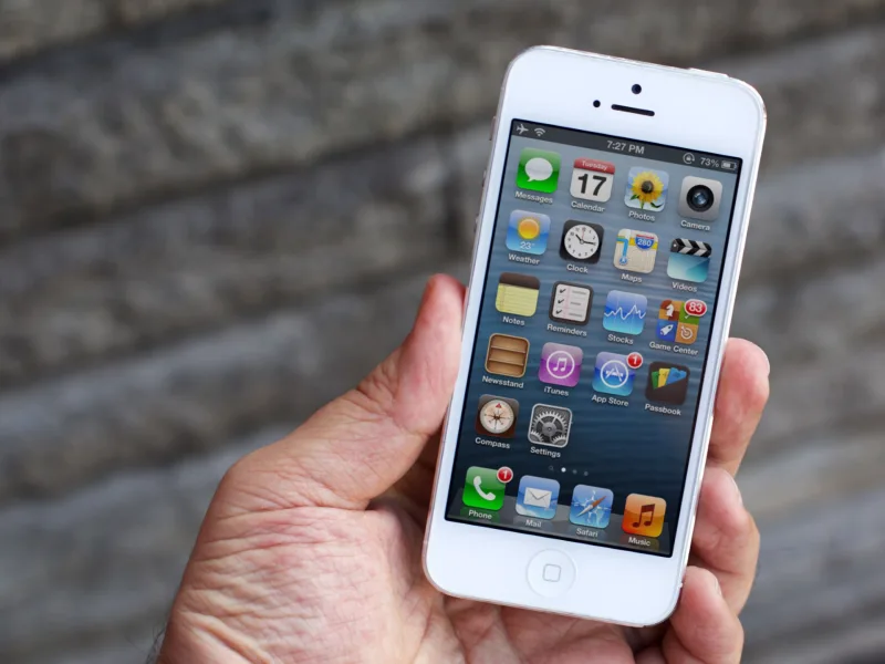 Λευκό iPhone 5 σε χέρι με φόντο πέτρινο τοίχο