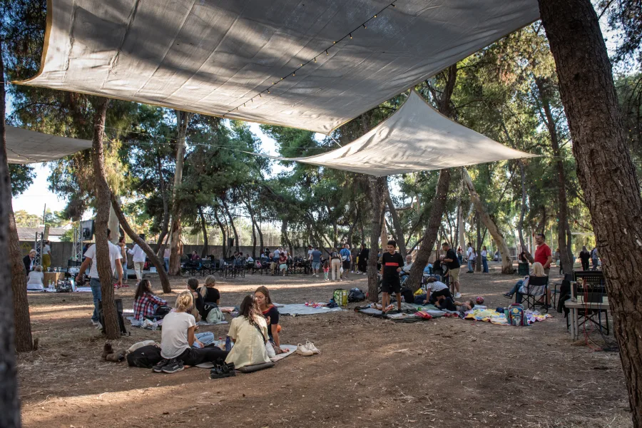 Κόσμος σε υπαίθριο φεστιβάλ κάτω από τέντες σε δασώδη περιοχή.