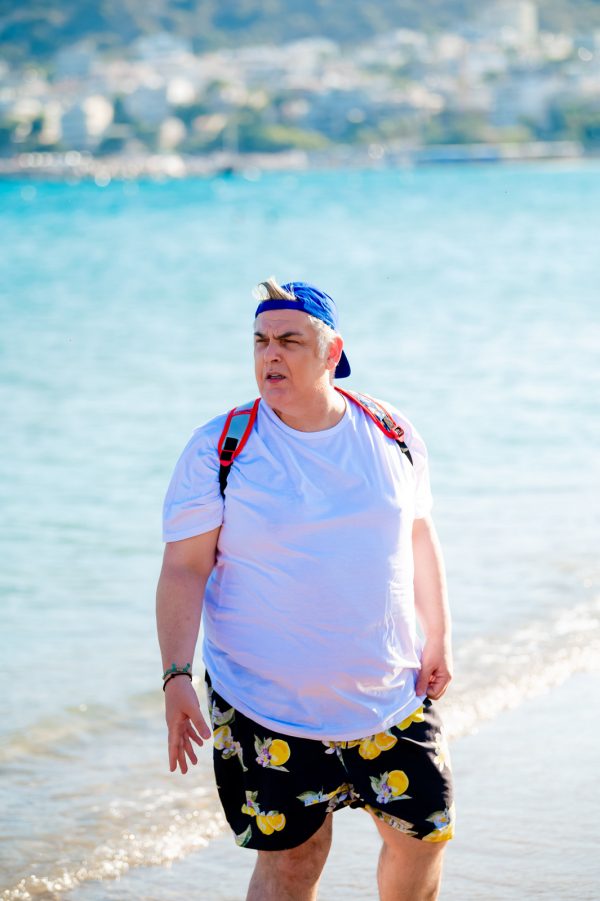 Άνδρας με λευκό t-shirt, μπλε καπέλο και σορτς με λεμόνια στην παραλία.