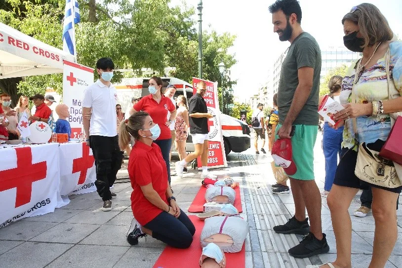 Εθελοντές του Ελληνικού Ερυθρού Σταυρού πραγματοποιούν επίδειξη πρώτων βοηθειών σε εξωτερικό χώρο.