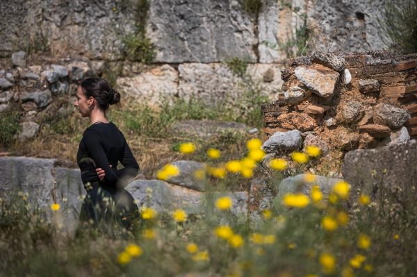 Καλλιτέχνης σε αρχαιολογικό χώρο με κίτρινα λουλούδια σε πρώτο πλάνο.