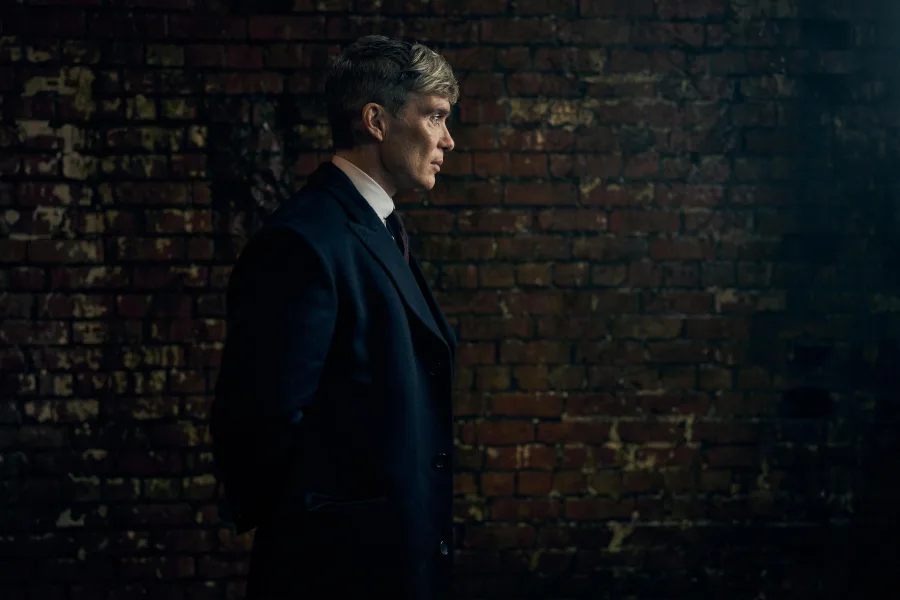 Ο Cillian Murphy ως Tommy Shelby, ο ηγέτης της συμμορίας Peaky Blinders, μπροστά σε έναν τοίχο από τούβλα.