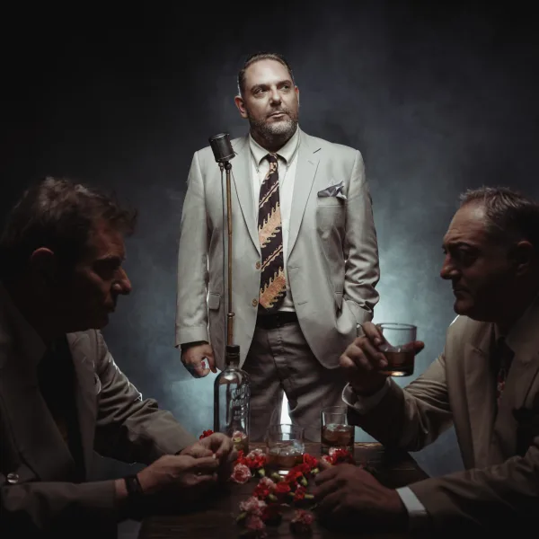 Τρεις άνδρες με κοστούμια σε σκηνικό που θυμίζει παλιό νυχτερινό κέντρο.