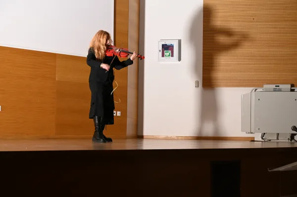 Μουσικός παίζει βιολί στη σκηνή κατά τη διάρκεια εκδήλωσης.