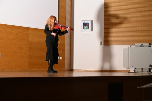 Μουσικός παίζει βιολί στη σκηνή κατά τη διάρκεια εκδήλωσης.