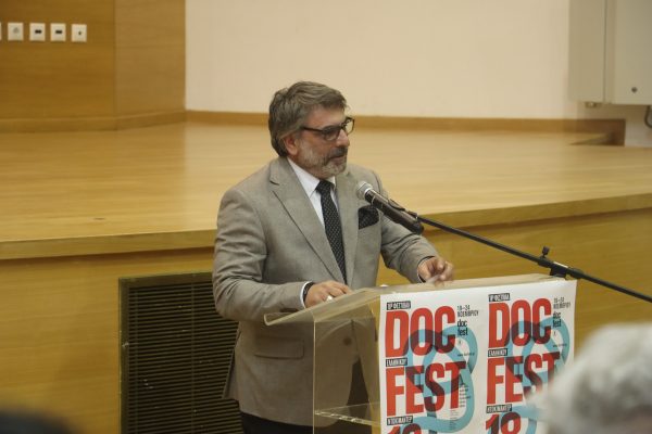 Άνδρας με κοστούμι μιλάει σε πόντιουμ στο 18ο Φεστιβάλ Ελληνικού Ντοκιμαντέρ.