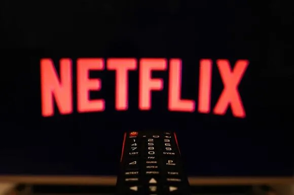 Το λογότυπο του Netflix σε οθόνη τηλεόρασης με ένα τηλεκοντρόλ σε πρώτο πλάνο.