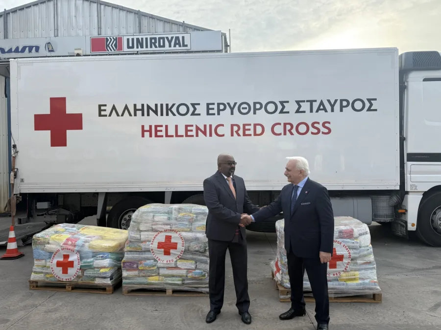 Δύο άνδρες κάνουν χειραψία μπροστά από φορτηγό του Ελληνικού Ερυθρού Σταυρού με ανθρωπιστική βοήθεια.