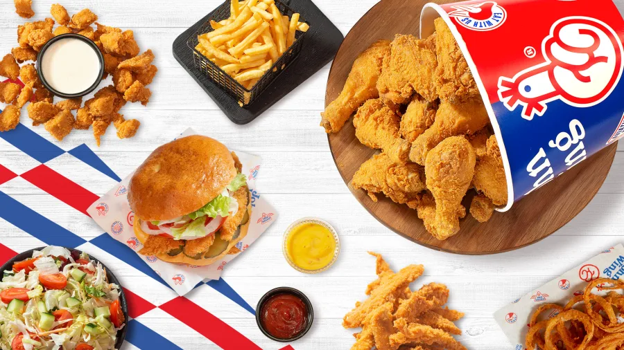 Ποικιλία από τηγανητό κοτόπουλο, burger, πατάτες, σαλάτα και σάλτσες σε ξύλινο τραπέζι.